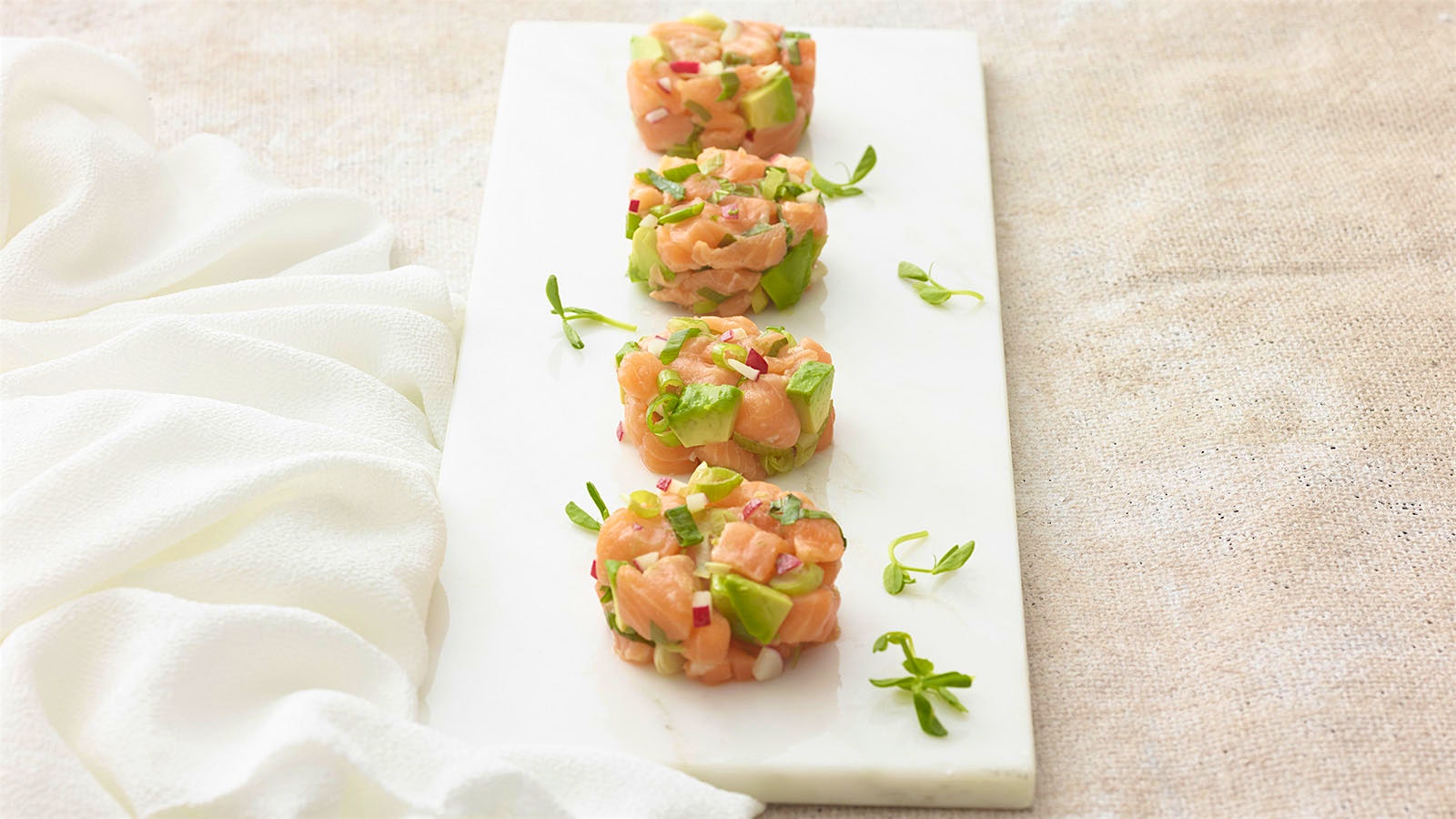 A serving plate with four discs of salmon and avocado tartare garnished with spring green